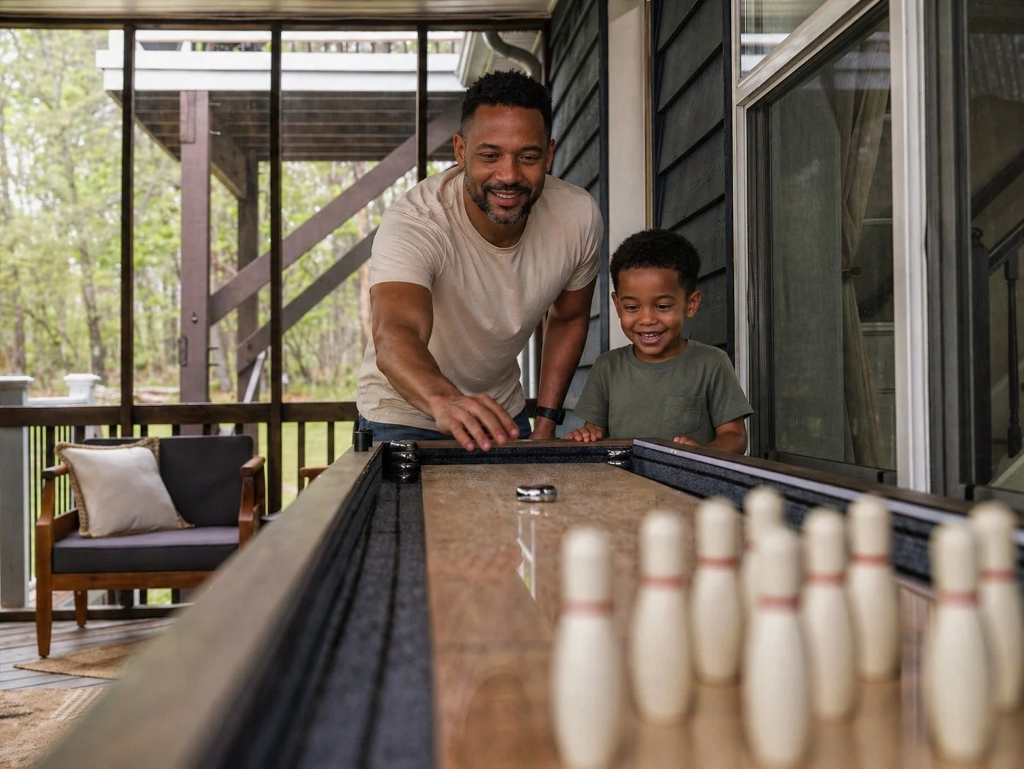 A guest and a young boy playing a tabletop shuffleboard game together on a screened porch