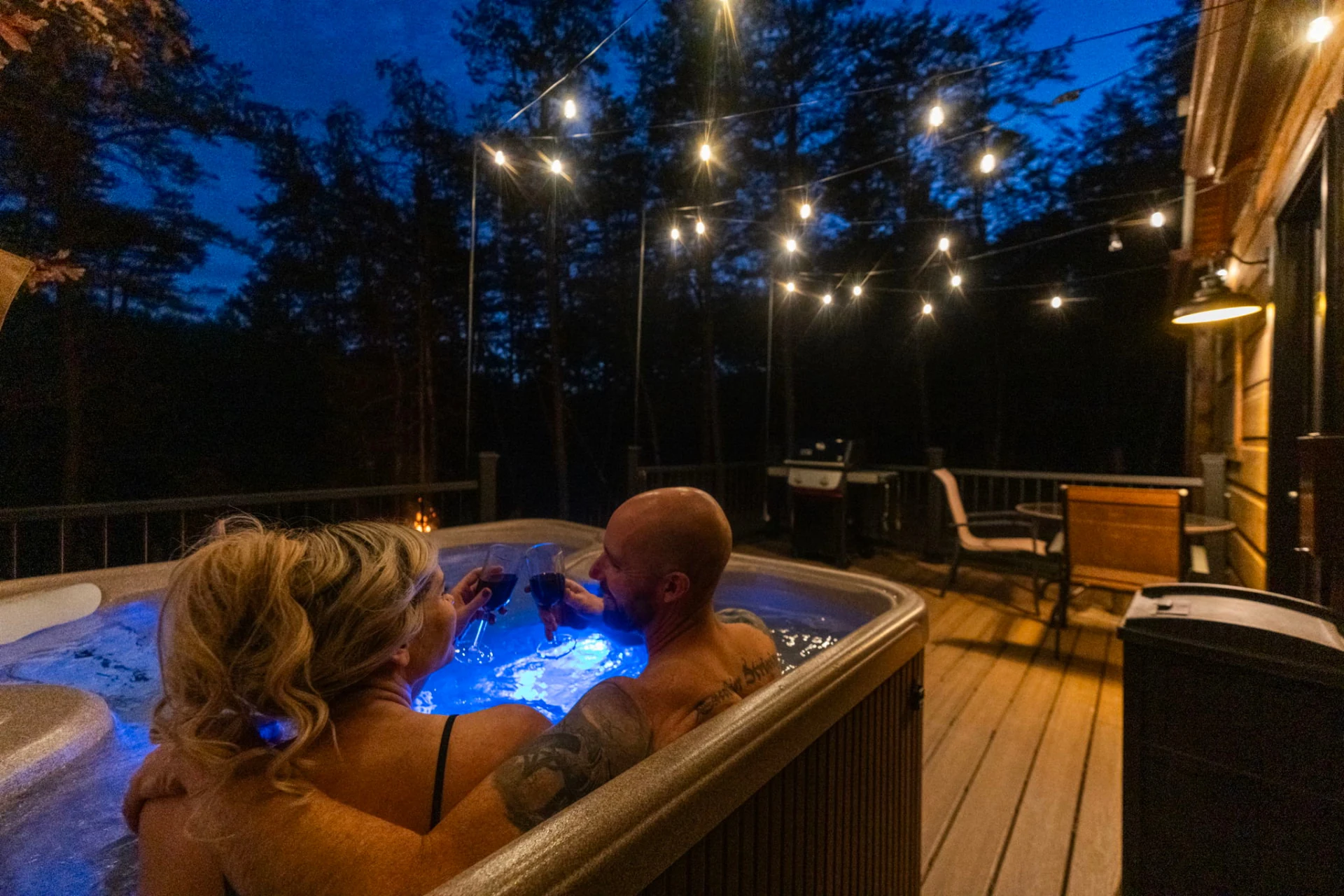 A couple toasting in a hot tub beneath evening string lights at Sky Mountain Retreat