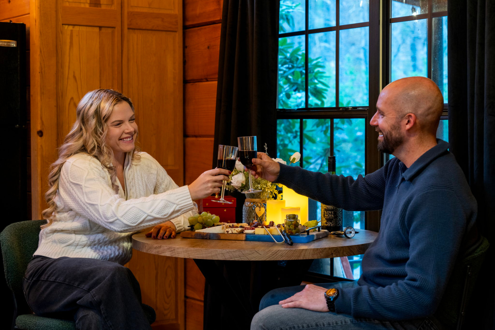 A couple toasting with glasses of red wine at a candlelit cabin table